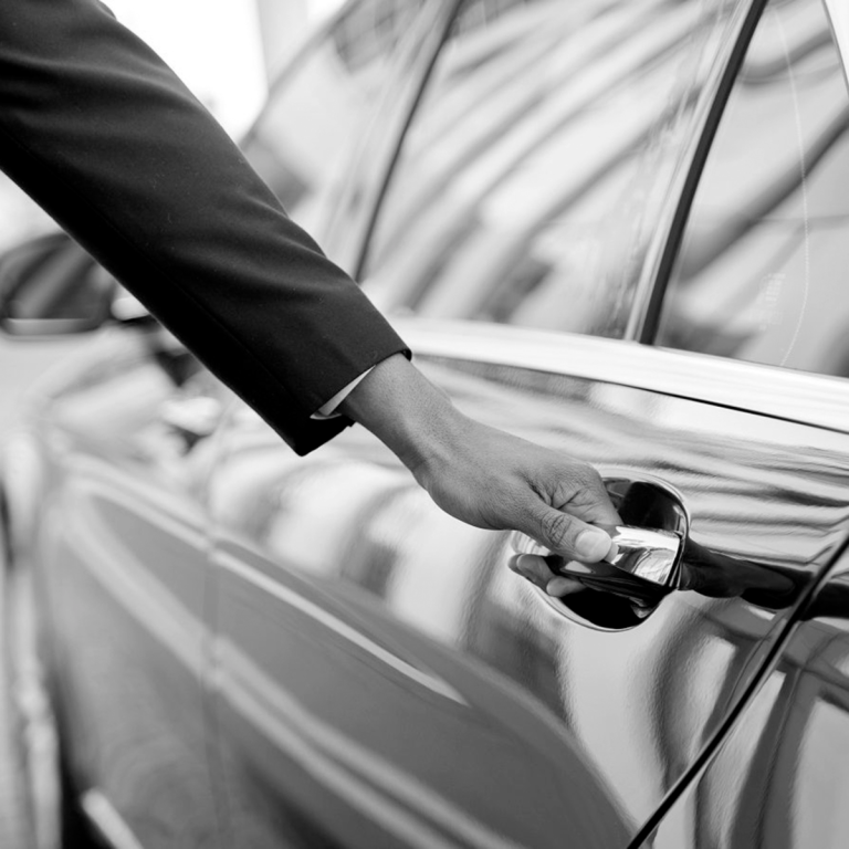 Main habillée en costume qui ouvre la portière d'une voiture noire.