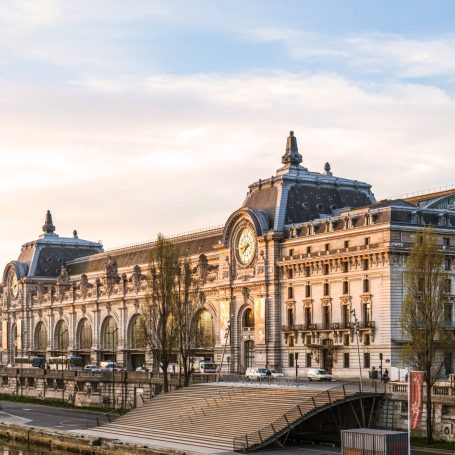 Ancienne gare ornée, aujourd'hui musée, au bord de la Seine à Paris sous un ciel clair.