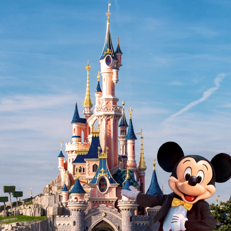 Mickey Mouse devant le château de Disney, décoré et coloré, sous un ciel bleu.