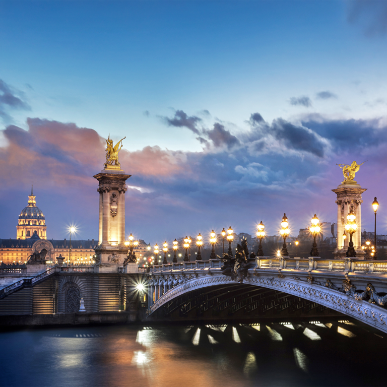 Pont Alexandre III à Paris, illuminé au crépuscule, avec des statues dorées et une vue sur la Seine.