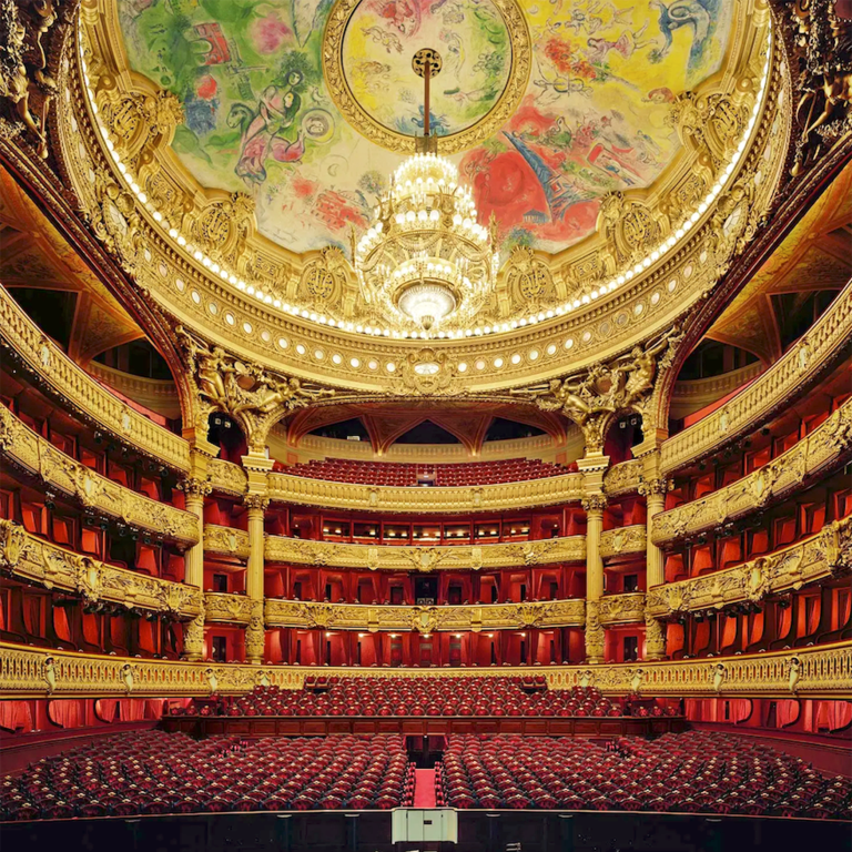 Intérieur d'un opéra majestueux avec un plafond décoré et des sièges rouges.