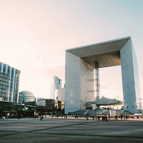 La Défense, Paris : grande arche moderne entourée de bâtiments et d'un ciel lumineux.