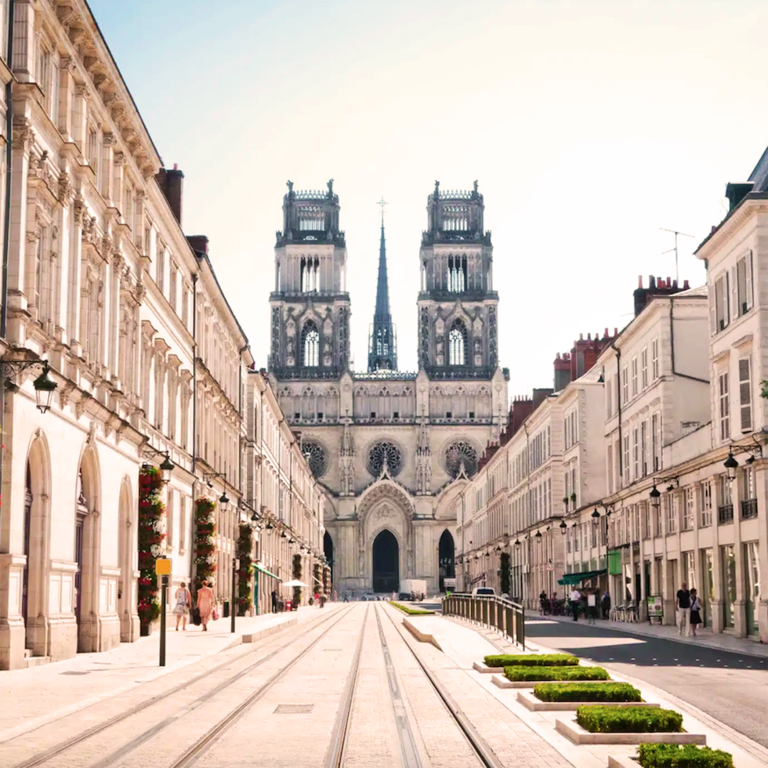 Vue d'une rue bordée de bâtiments, avec la cathédrale d'Orléans en arrière-plan.
