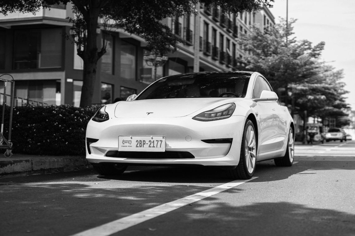 Voiture électrique blanche garée sur une rue bordée d'arbres.