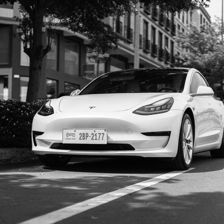 Voiture électrique Tesla Model 3 blanche garée sur une rue avec des bâtiments en arrière-plan.