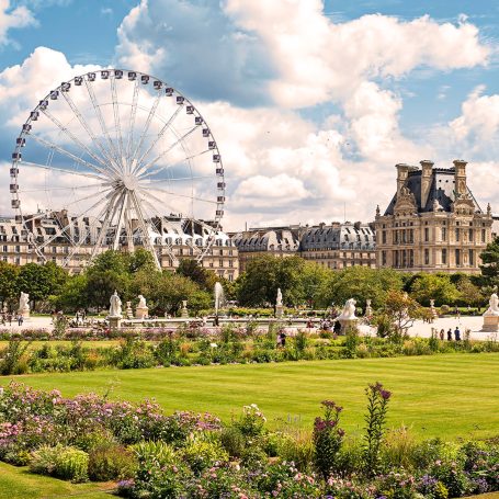 Vue des jardins du Louvre avec la grande roue en arrière-plan et des nuages dans le ciel.