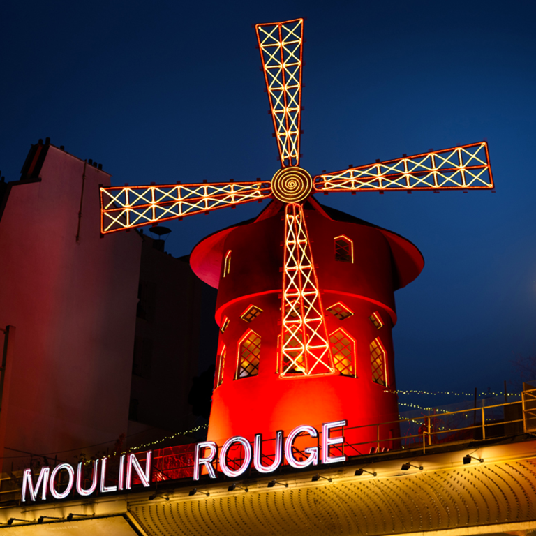 Moulin Rouge illuminé la nuit avec un grand moulin à vent au sommet.
