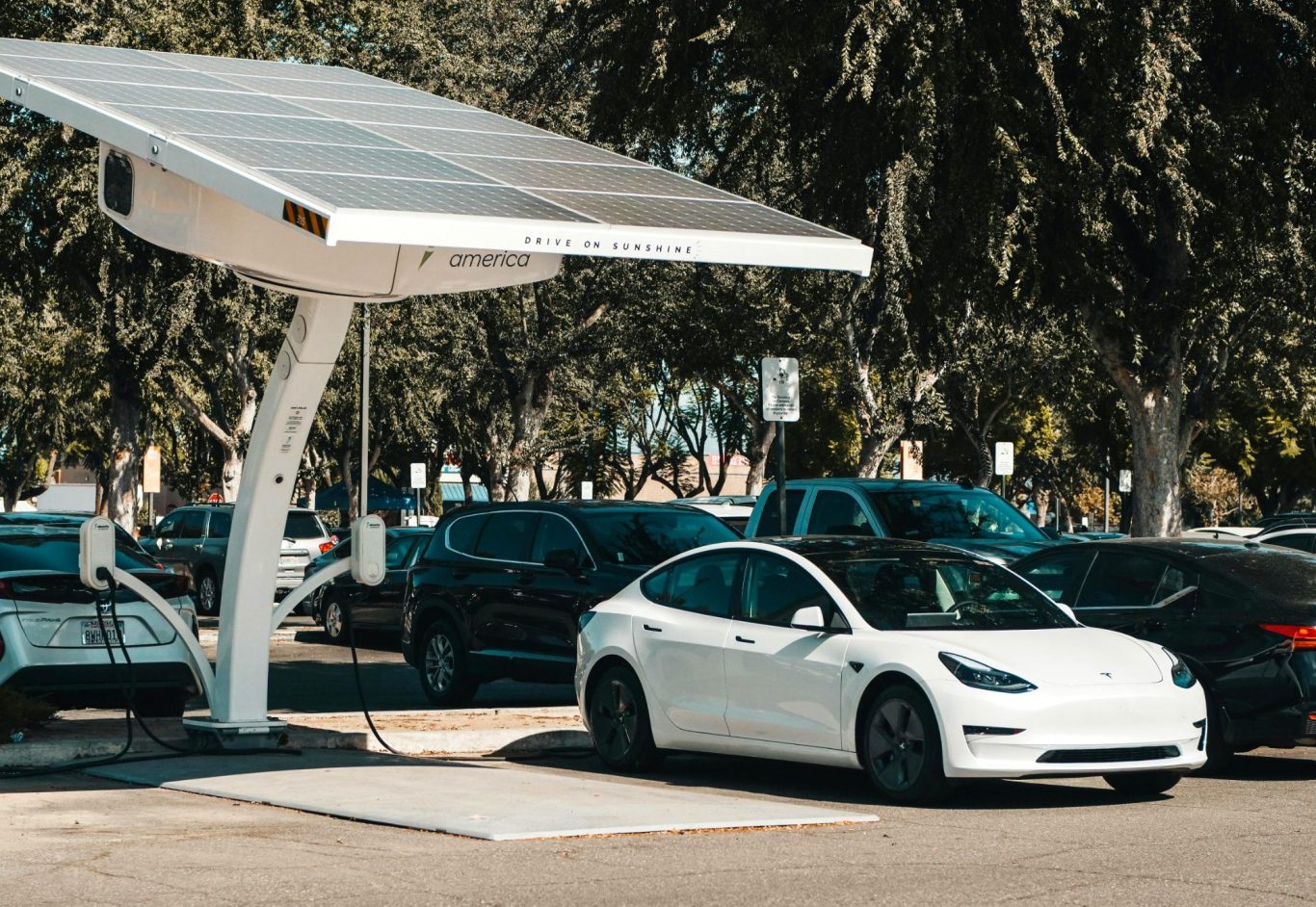Voiture électrique blanche stationnée sous un panneau solaire dans un parking.