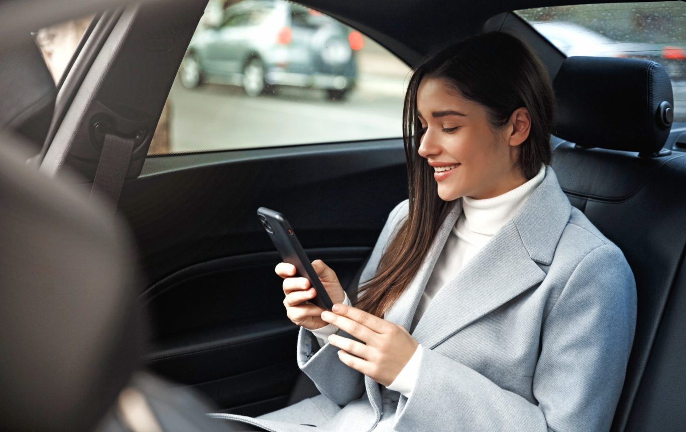 Femme souriante utilisant son téléphone à l'arrière d'une voiture.