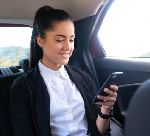 Femme souriante utilisant son téléphone à l'arrière d'une voiture.