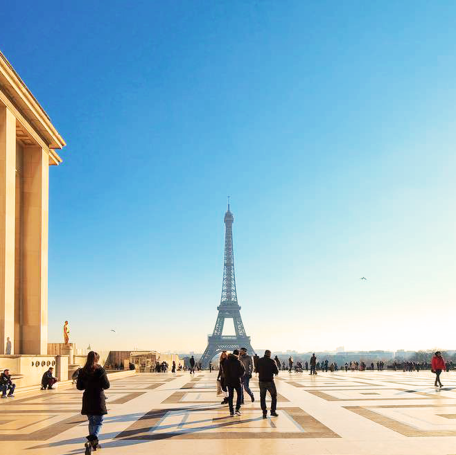 Vue sur la tour Eiffel avec des personnes se promenant sous un ciel bleu clair.