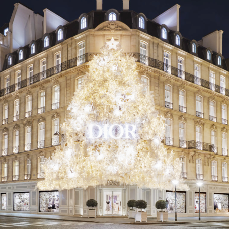 Façade illuminée d'un magasin Dior, décorée d'un grand sapin de Noël scintillant.