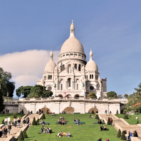Basilique du Sacré-Cœur sur la butte Montmartre, entourée de verdure et de visiteurs.