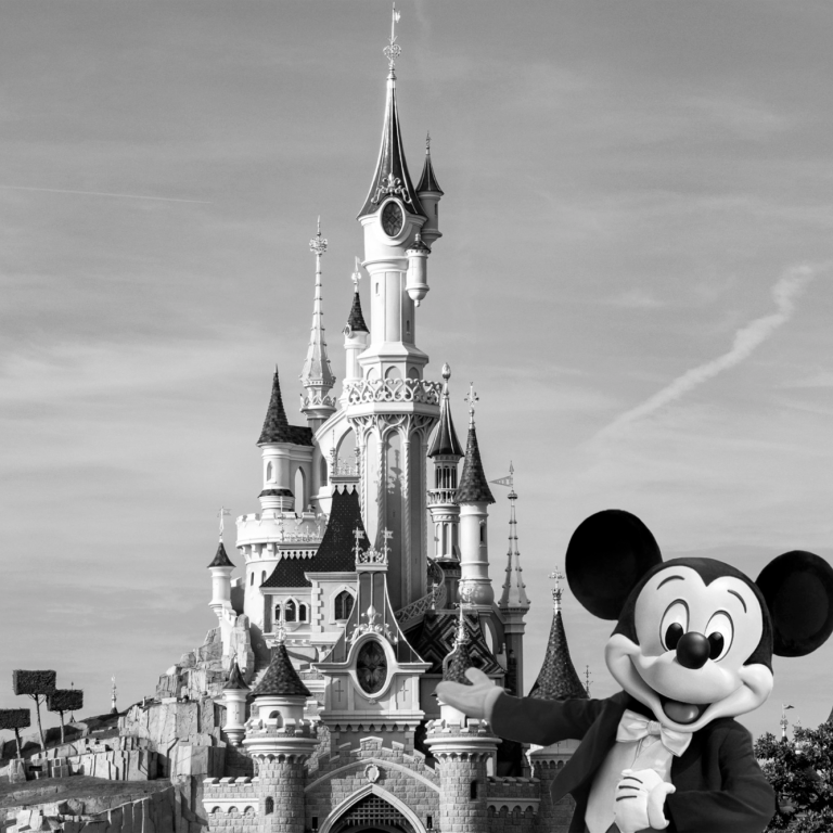 Mickey Mouse pose devant un château féerique en noir et blanc.