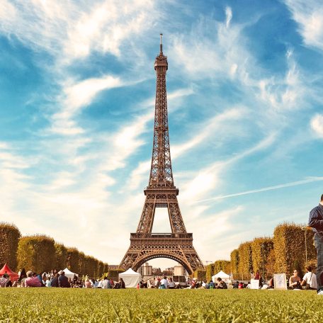 Tour Eiffel entourée de visiteurs dans un parc, ciel bleu avec quelques nuages.