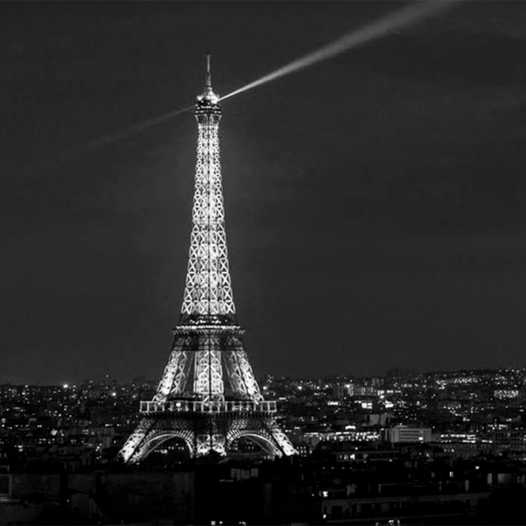 Tour Eiffel illuminée, rayons lumineux perçant le ciel nocturne de Paris.